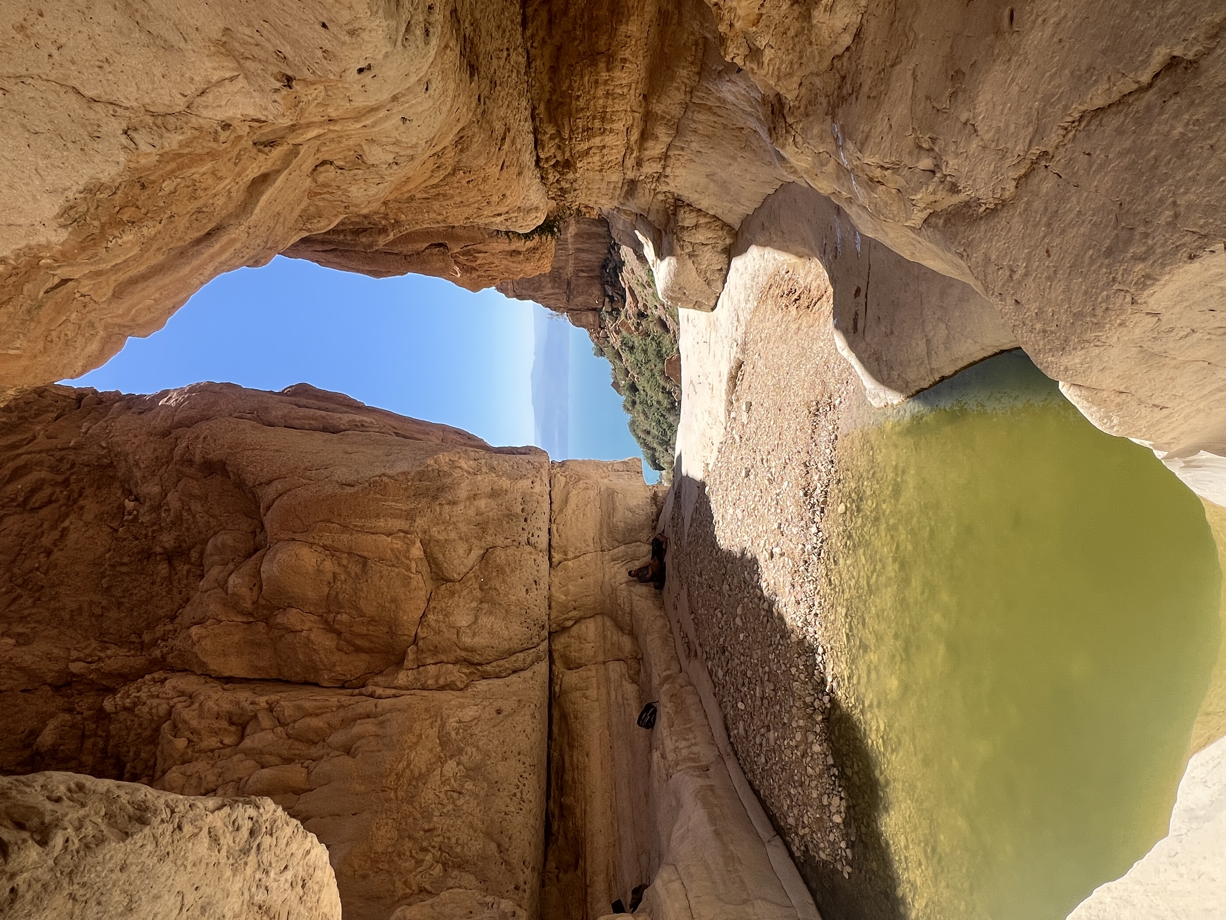 Natural rock arch opening to blue sky with green pool below, Gev Chalon, Dead Sea