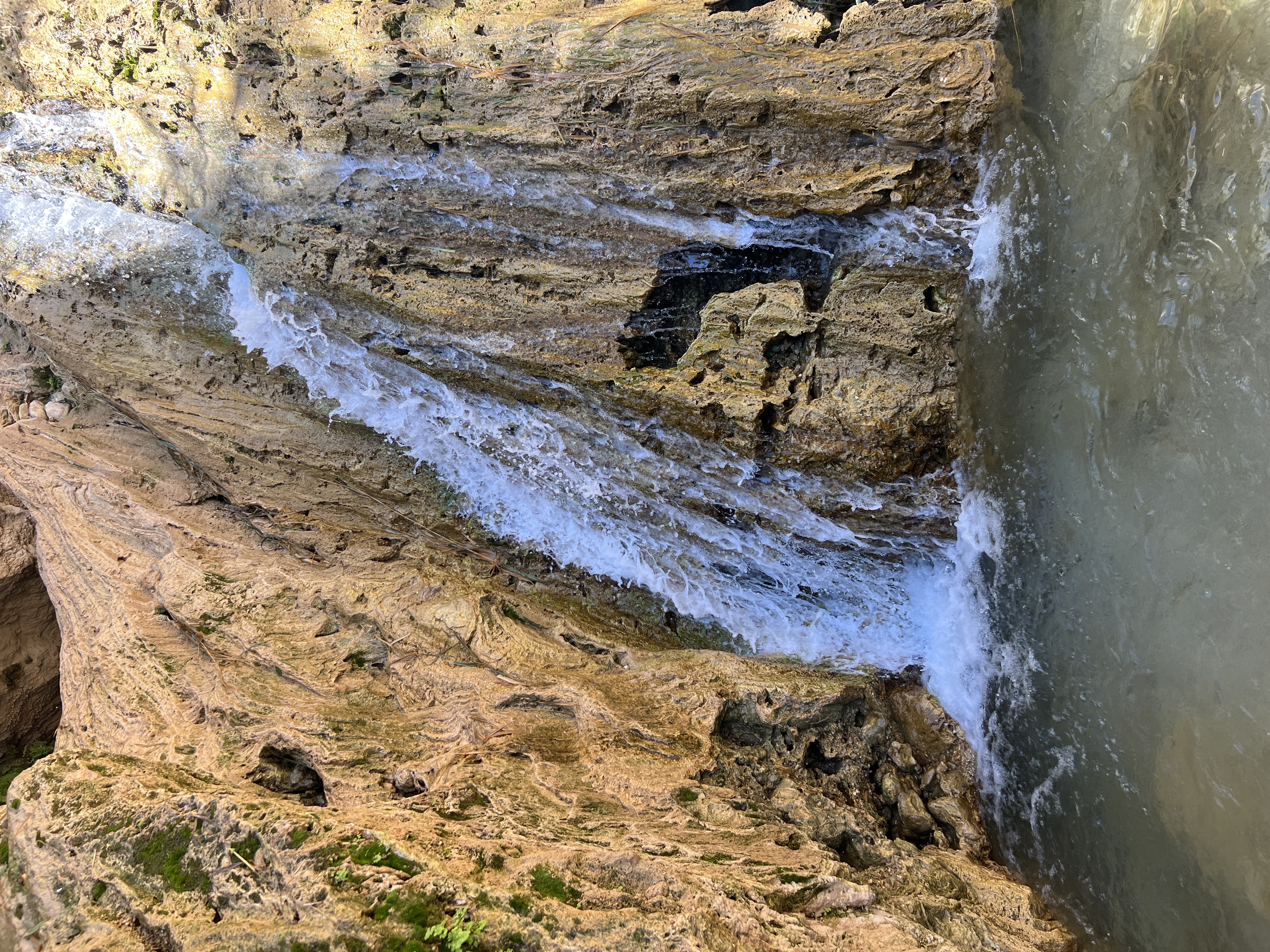 Waterfall flowing over smooth layered rock inside Dodim Cave, Ein Gedi