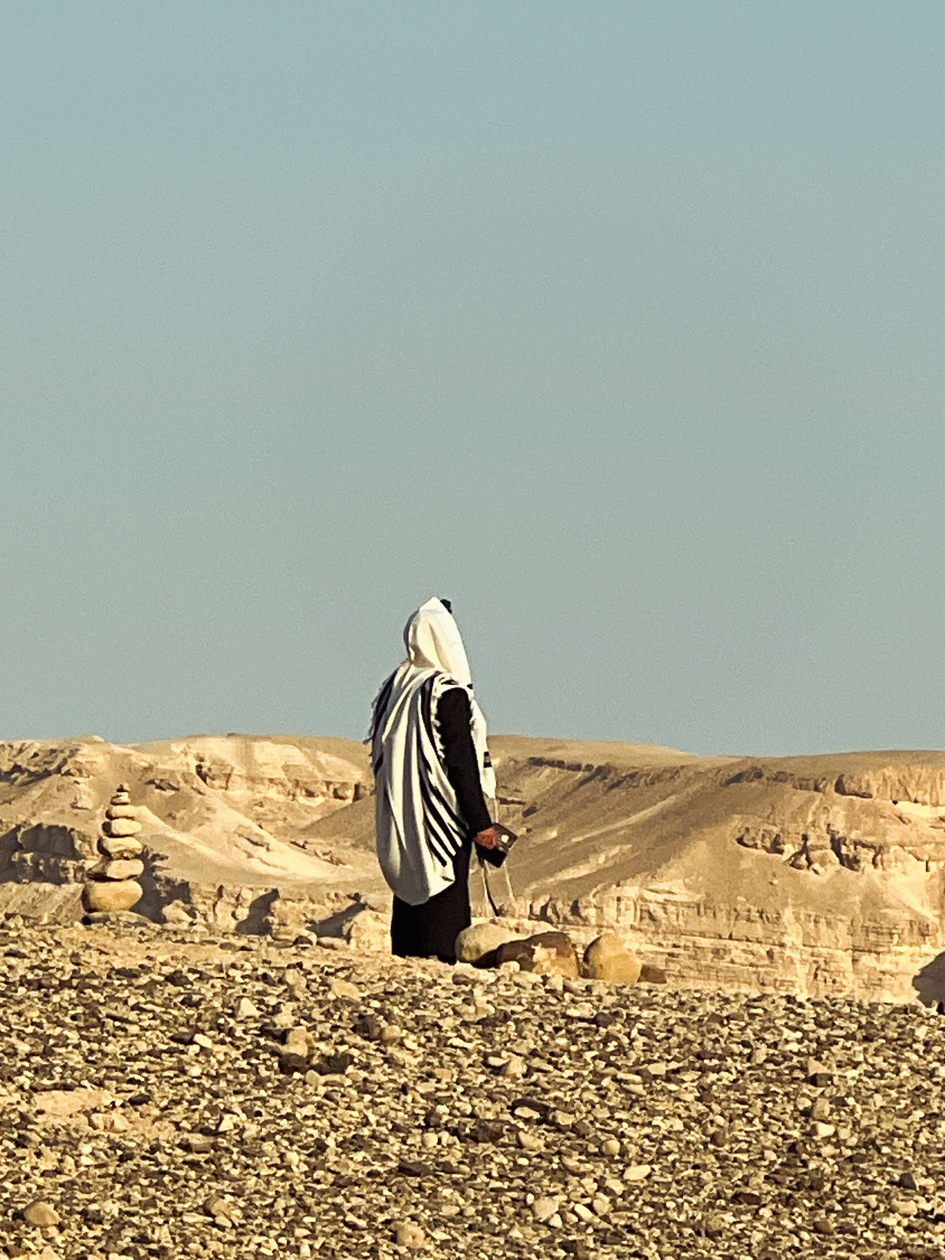 Jewish man wearing tallit prayer shawl standing alone on rocky ground in the Judean Desert, golden hour light