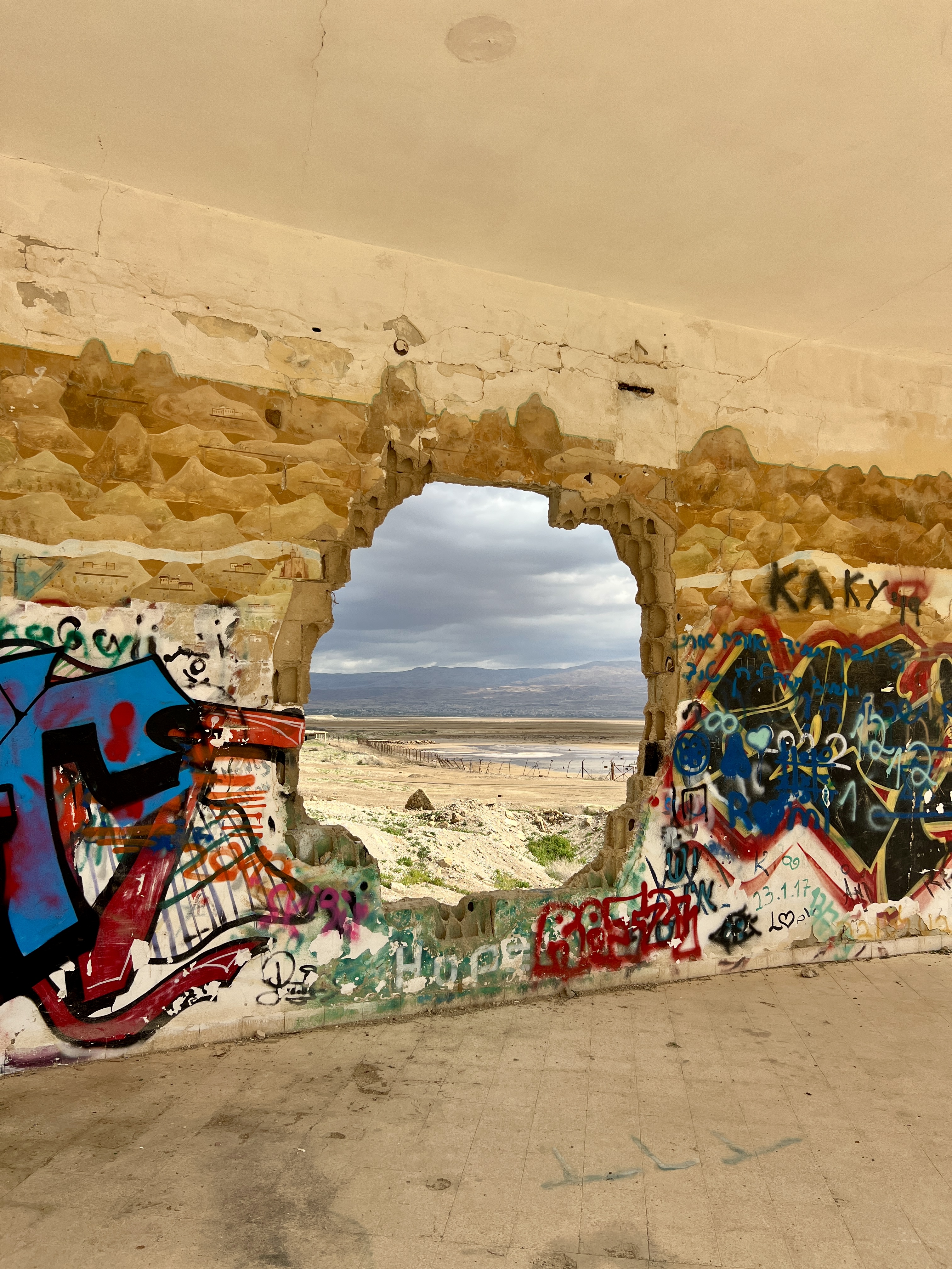 Colorful graffiti on ruined wall with large hole revealing beach and sea beyond, abandoned building Israel